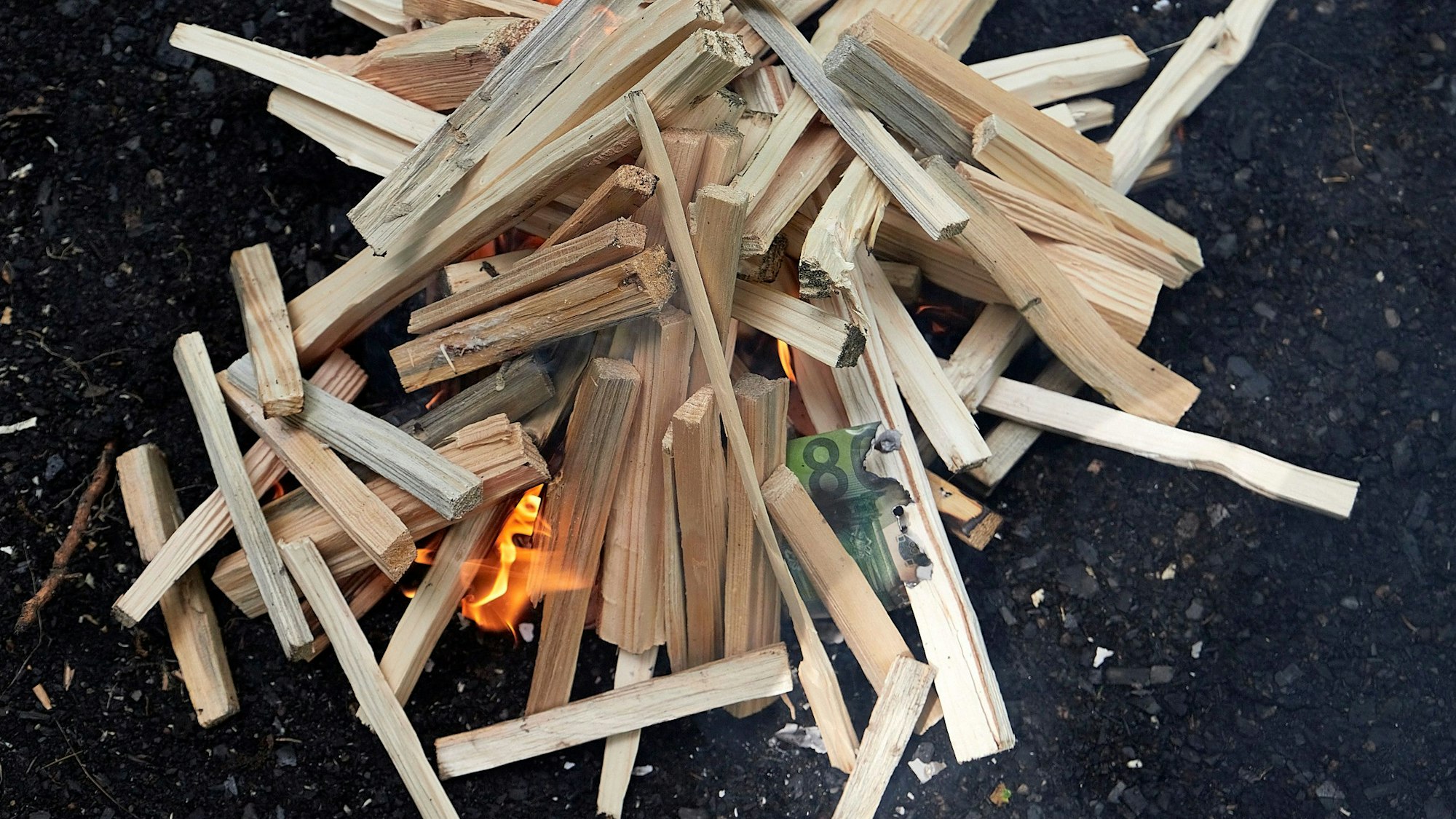 Kleine Buchenscheite liegen auf schwarzer Kohle und brennen.