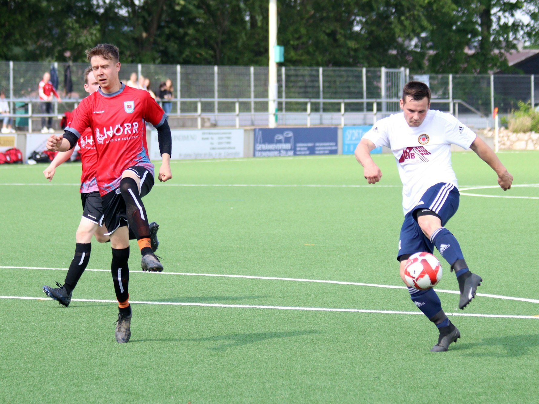 Ein Fußballer beim Schuss, ein Gegner streckt abwehrend das Bein aus.