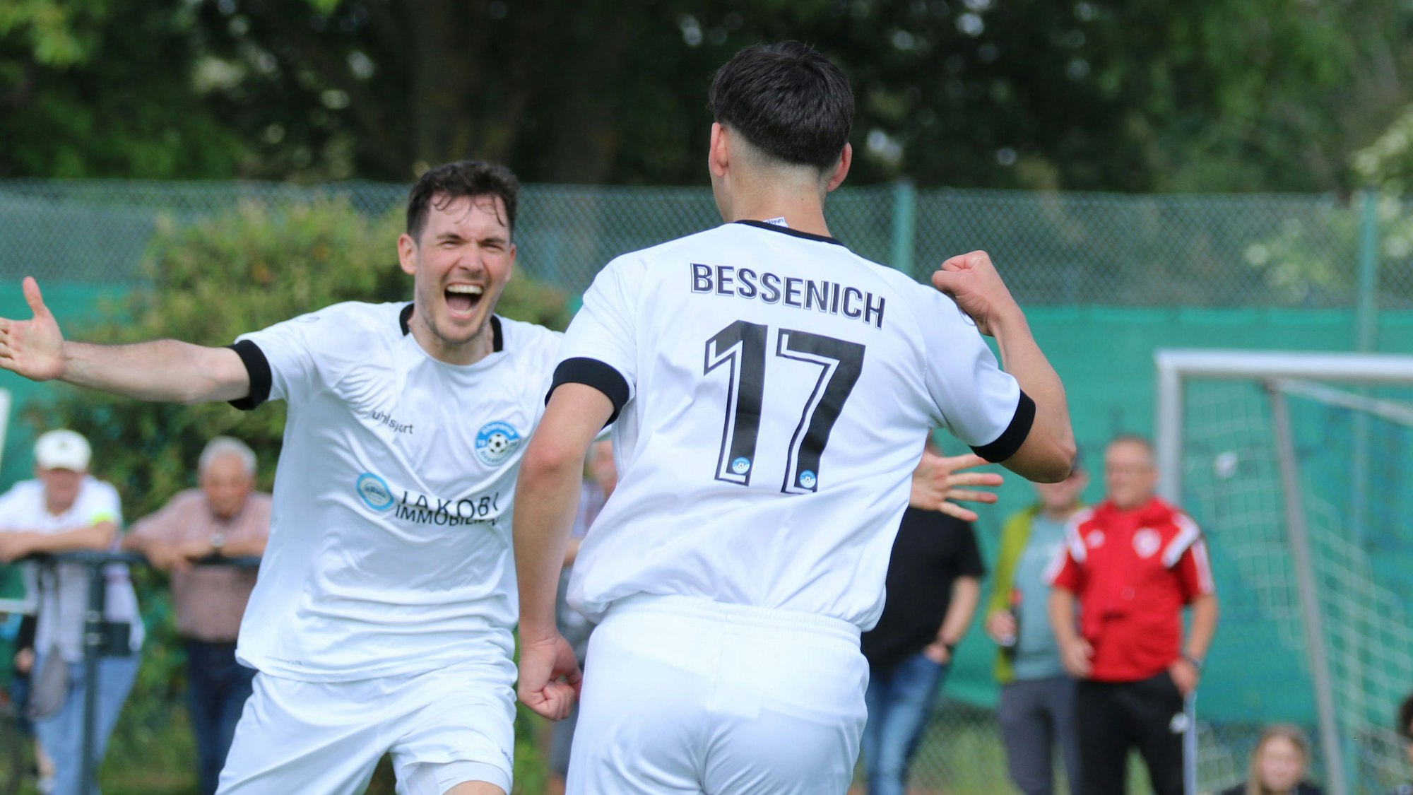 Zwei Fußballer jubeln: Einer mit ausgebreiteten Armen, ein anderer mit erhobener Faust.