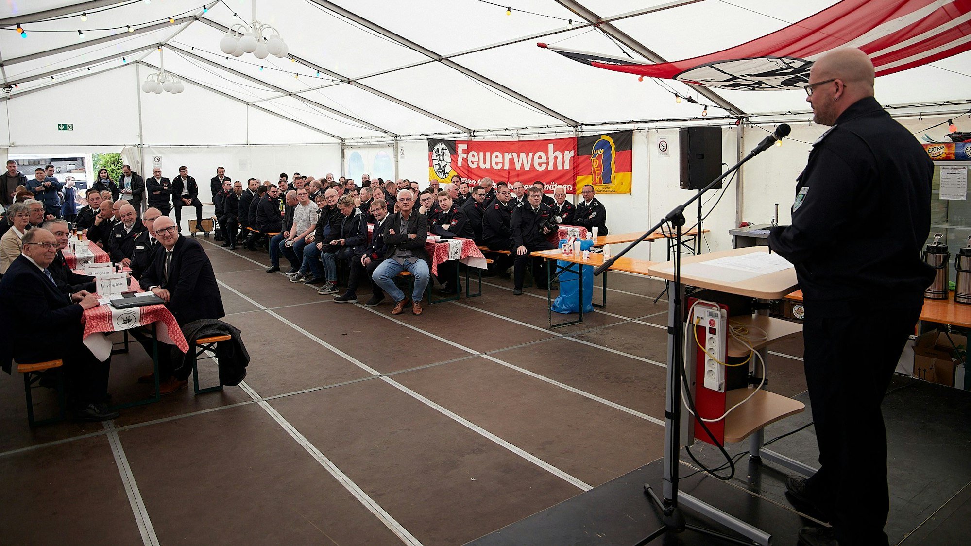 Das Bild zeigt einen Blick ins Festzelt. Auf der Bühne steht am Mikrofon ein Redner.