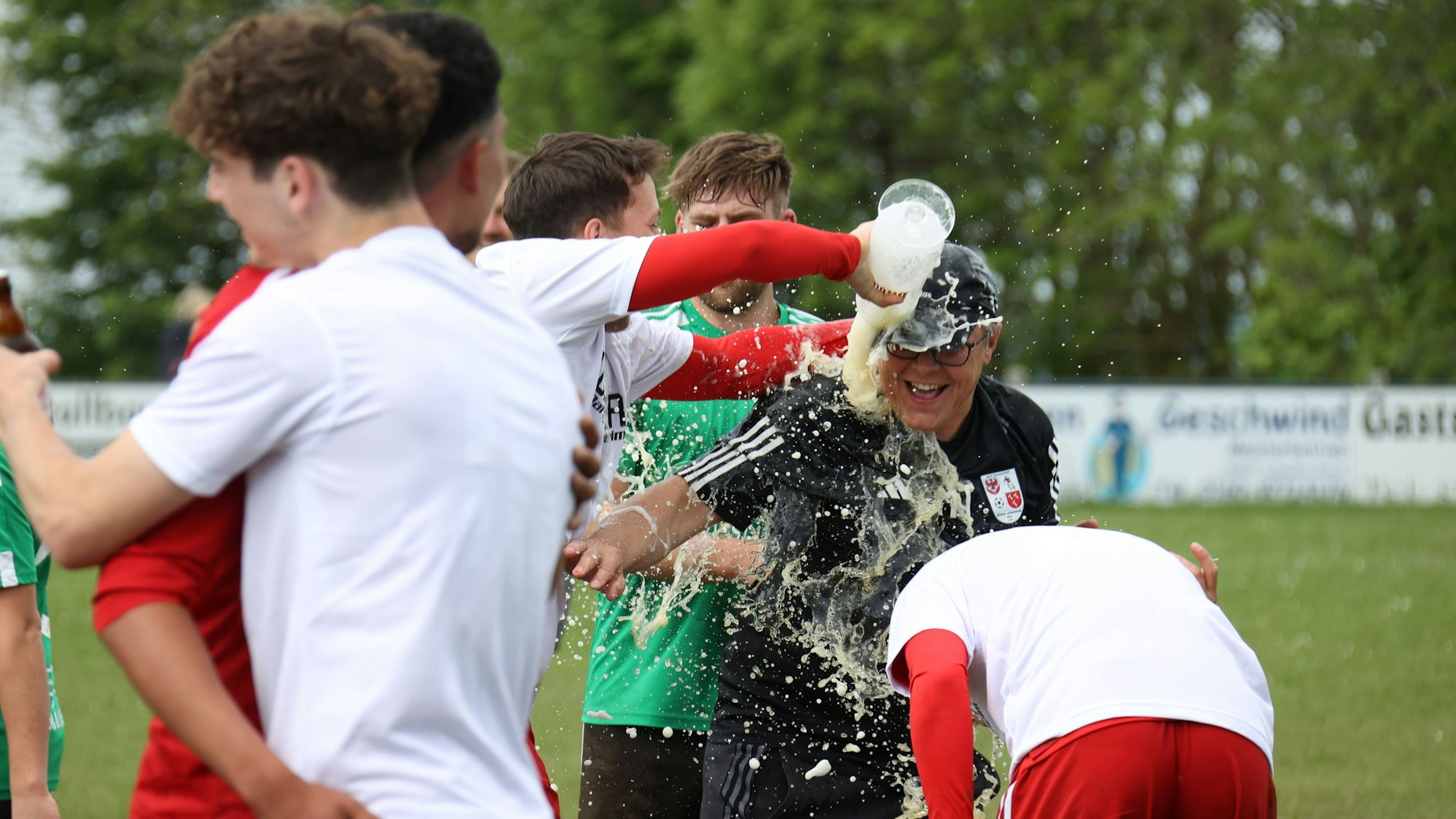 Ein Fußballer kippt ein Glas Bier über seinen Trainer.
