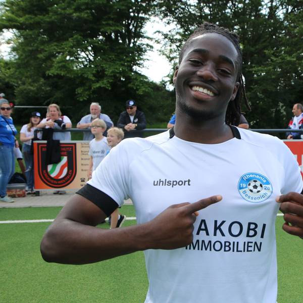 Samson Sayongo zeigt mit ausgestrecktem Finger auf das Bessenich-Logo.