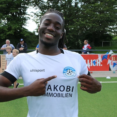 Samson Sayongo zeigt mit ausgestrecktem Finger auf das Bessenich-Logo.