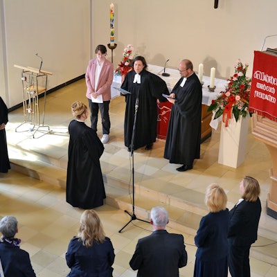 Pfarrerin Dorothee Lindenbaum steht vor Superintendentin Claudia Müller-Bück, die Presbyter bilden einen Halbkreis darum.