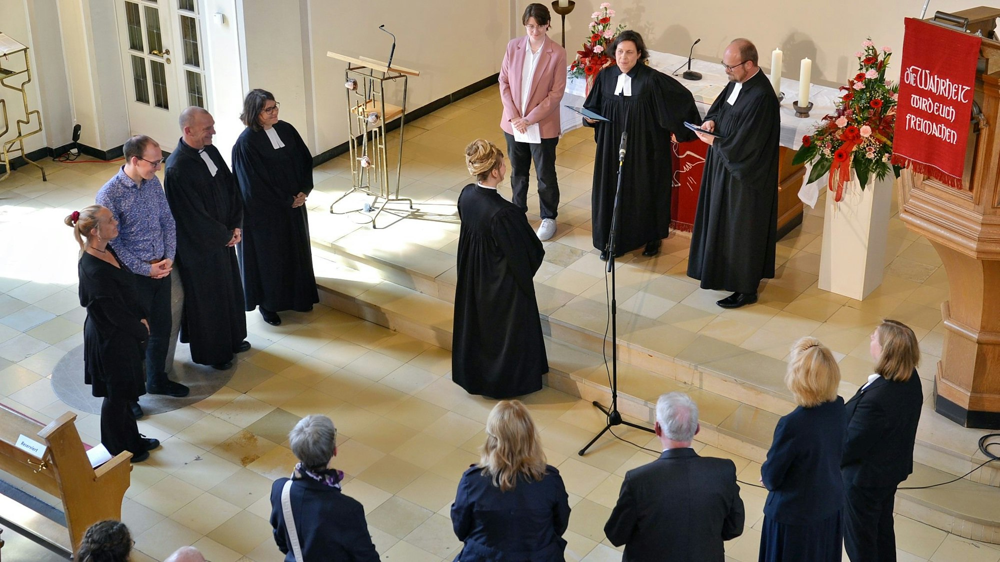Pfarrerin Dorothee Lindenbaum steht vor Superintendentin Claudia Müller-Bück, die Presbyter bilden einen Halbkreis darum.