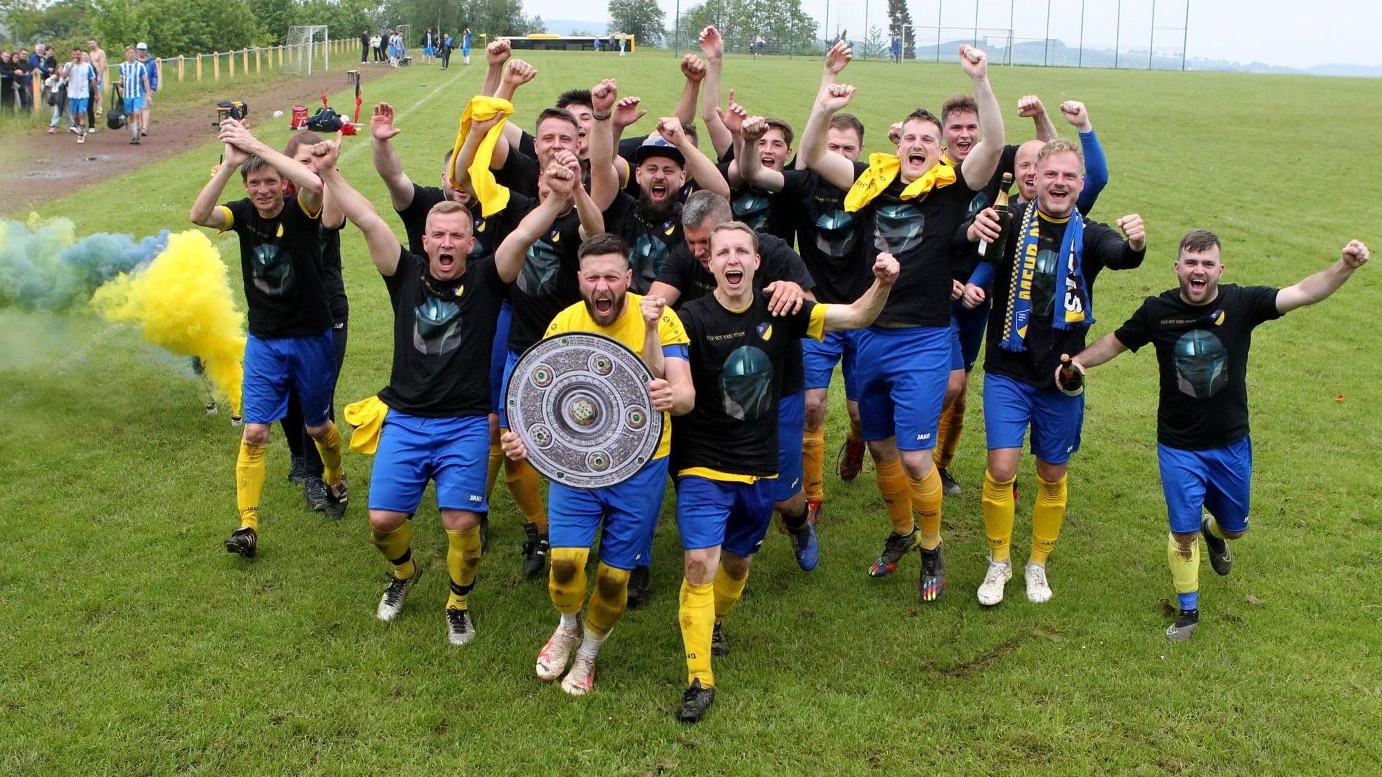 Ein Team feiert mit einer Meisterschale den Aufstieg.