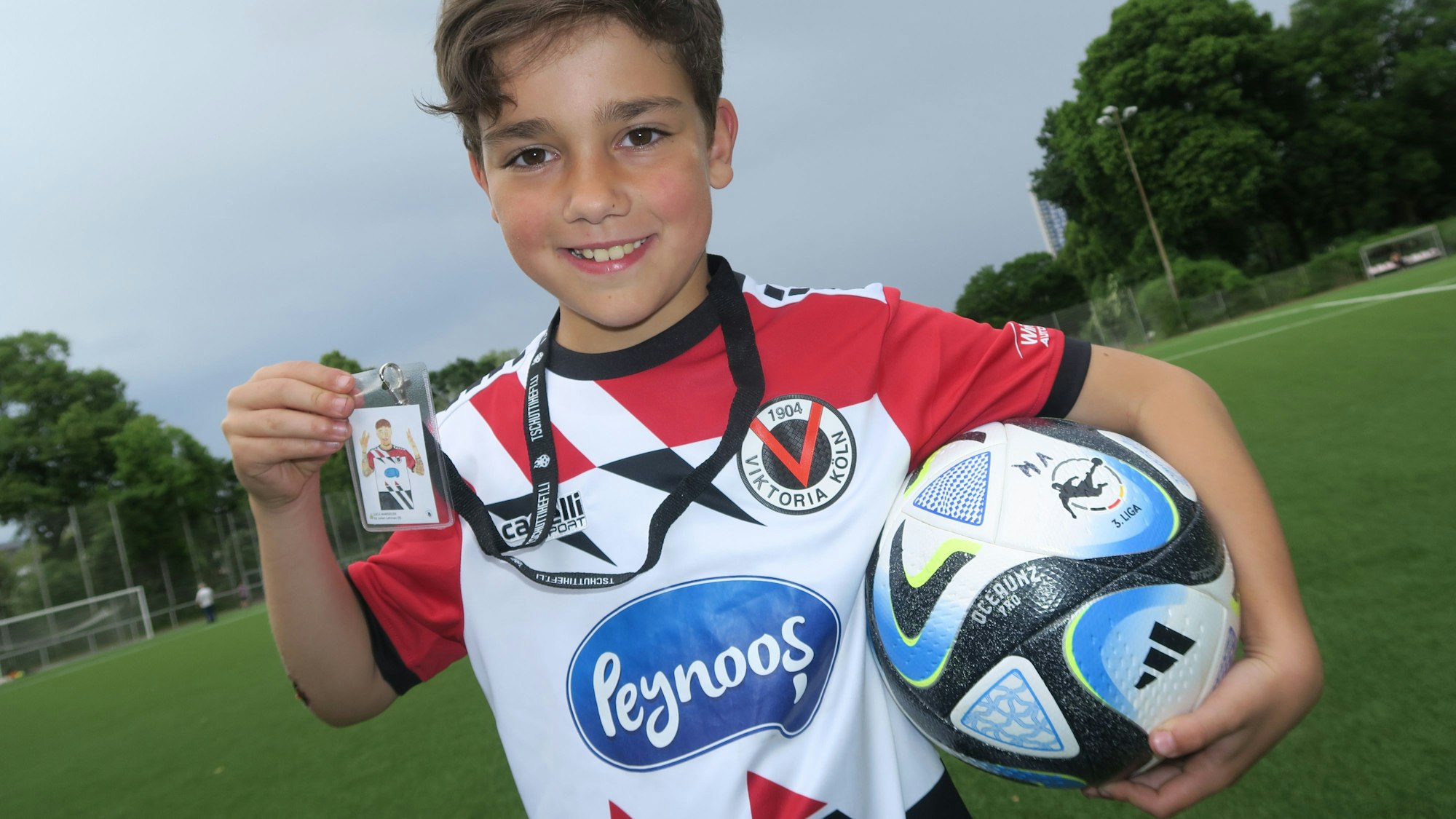 Auf den Fotos ist Julian Lehmann mit seinem "Sticker"-Bild von Luca Marseiler auf dem Kunstrasenplatz von Eintracht Köln zu sehen.