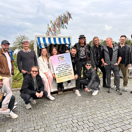 Die Veranstalter von Sommer Sonne Alaaf sowie die Bands Lupo und Domstürmer posieren vor einem Maibaum im Seepark.