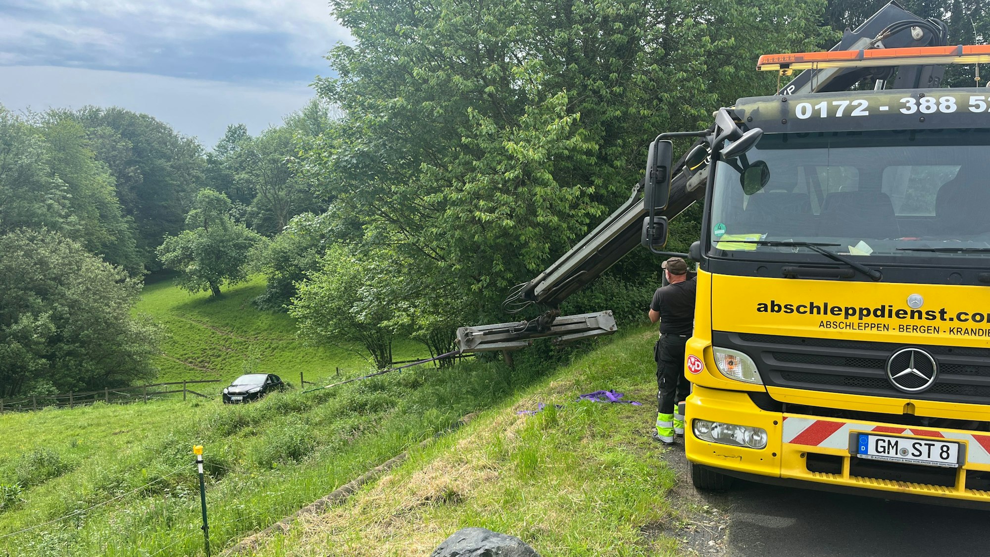 Ein Abschleppunternehmer zieht mit seinem Kranfahrzeug das Auto über den Hang nach oben.