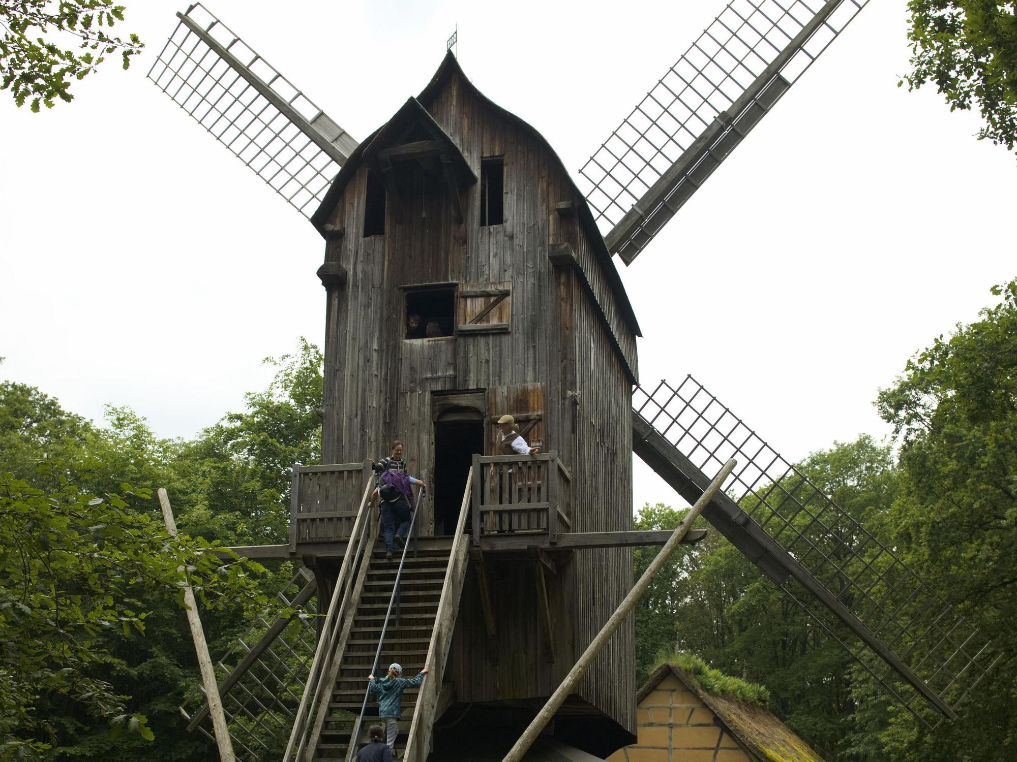 Drei Besucher steigen die Stufen der Bockwindmühle hoch.