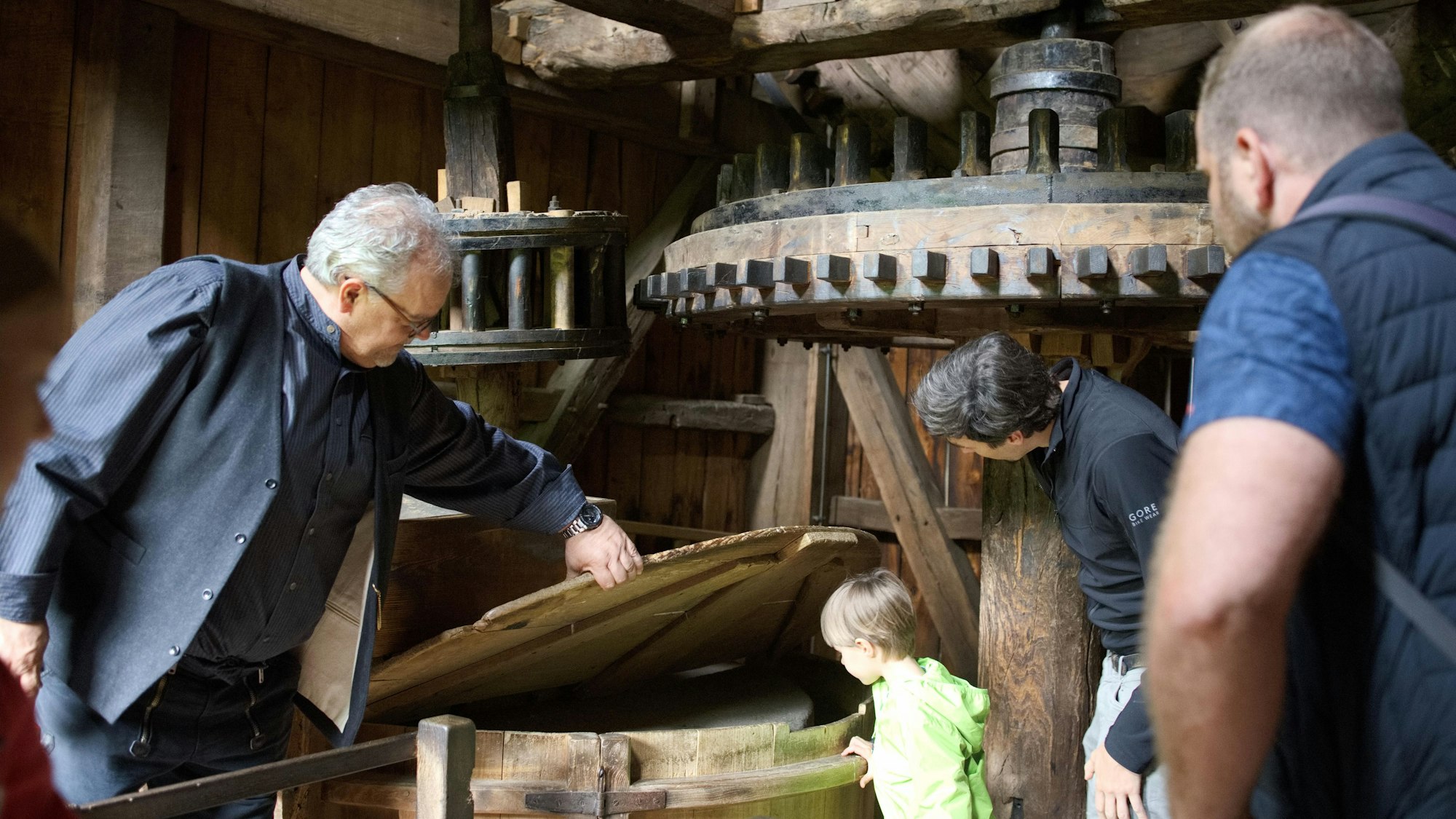 Ein Mann hebt einen Deckel hoch, ein Kind schaut interessiert hinein. In etwas Entfernung stehen Männer.