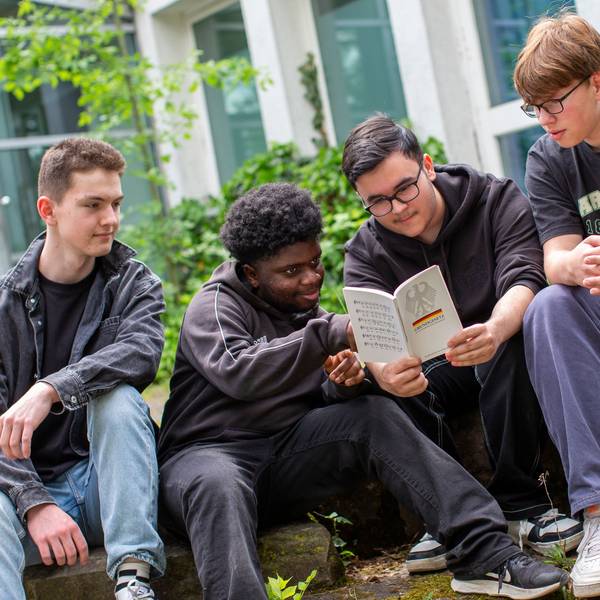 Vier 16-jährige Jungen sitzen nebeneinander und schauen auf ein aufgeschlagenes Grundgesetz.