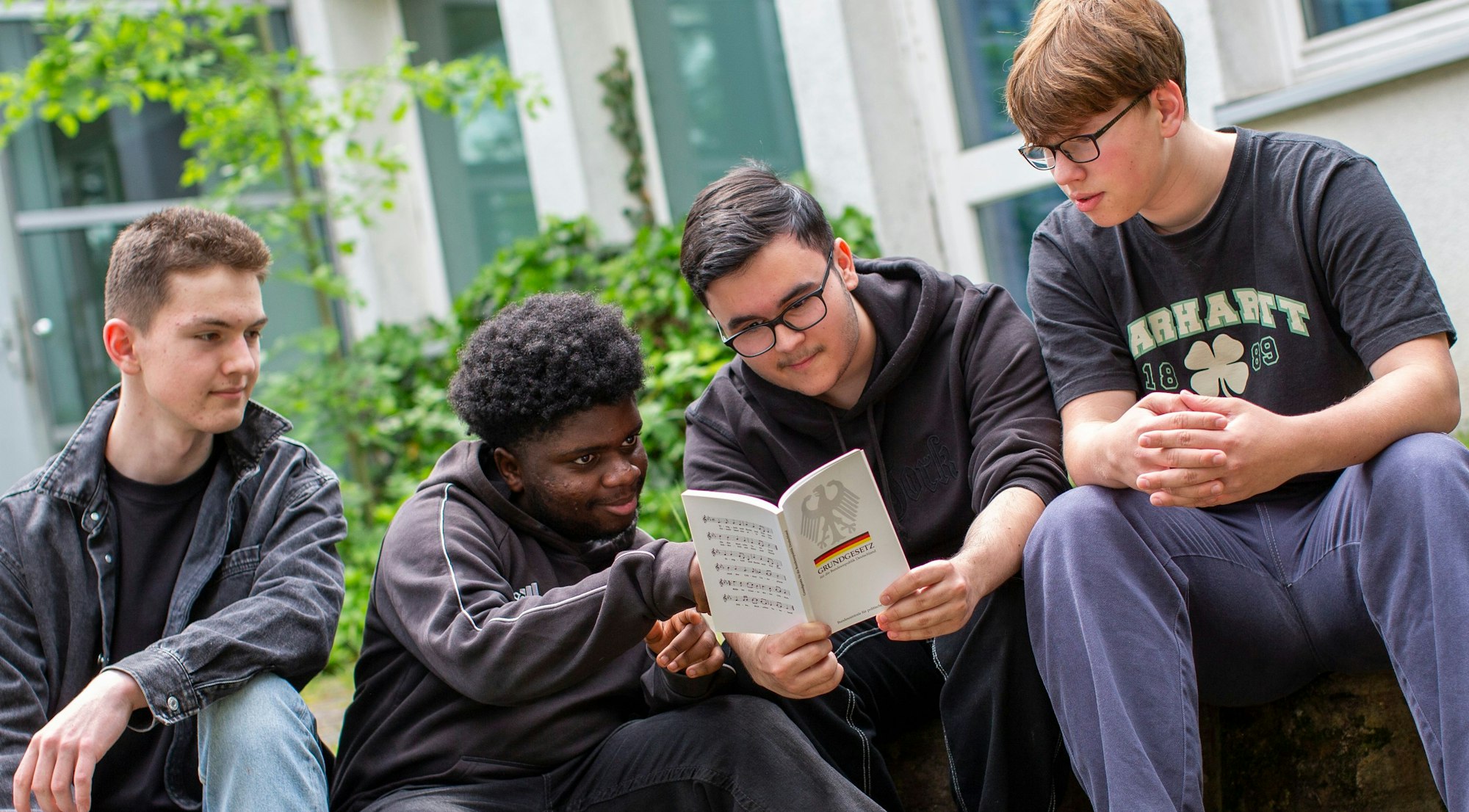 Vier 16-jährige Jungen sitzen nebeneinander und schauen auf ein aufgeschlagenes Grundgesetz.