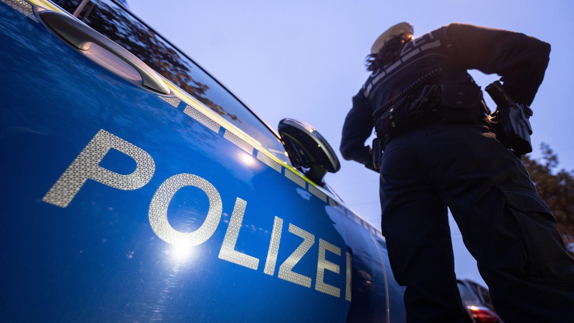 Auf dem Foto ist eine Polizistin zu sehen, die neben einem Streifenwagen steht.