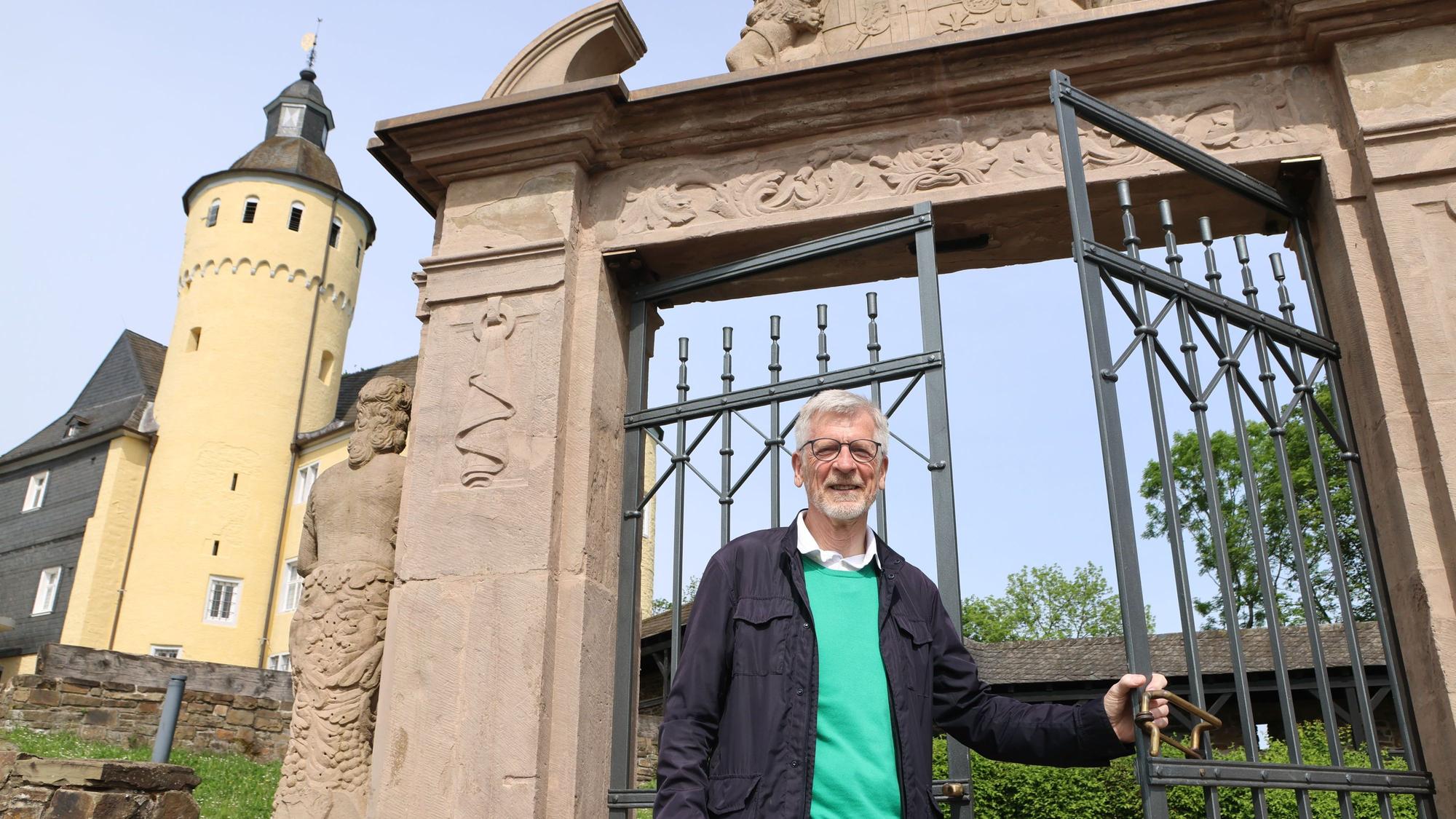 Ein Mann steht an einem Metalltor, dahinter ragt der Schlossturm auf.