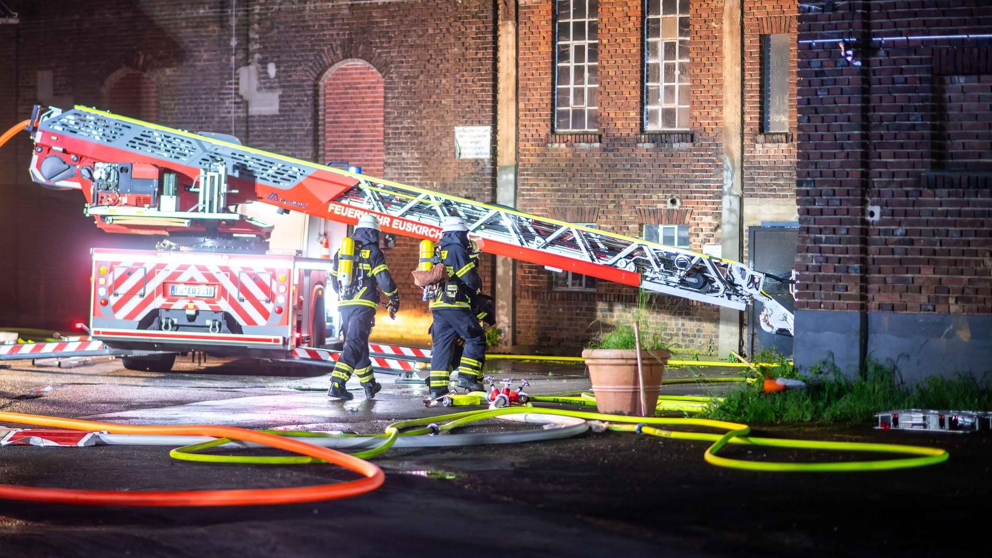 Das Bild zeigt die Drehleiter der Euskirchener Feuerwehr. Zwei Feuerwehrleute gehen unter Atemschutz in Richtung Lagerhalle.