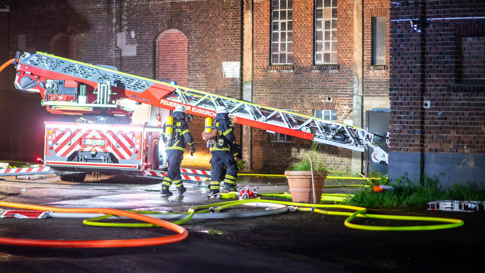 Das Bild zeigt die Drehleiter der Euskirchener Feuerwehr. Zwei Feuerwehrleute gehen unter Atemschutz in Richtung Lagerhalle.