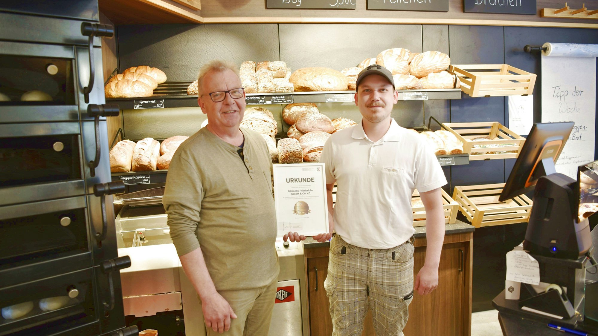 Klemens und Alexander Friederichs präsentieren im Verkaufsraum ihrer Bäckerei ihre Urkunde.