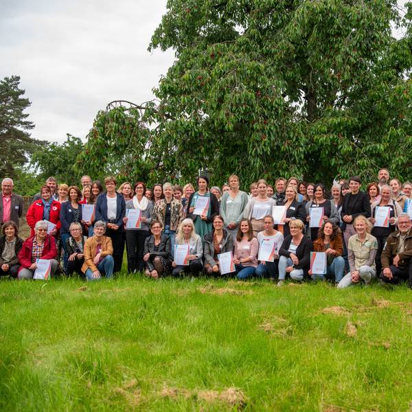 Eine Gruppe von Menschen steht auf einer Wiese unter einem Kirschbaum, mit dabei Josefine Paul (Grüne) Landesministerin für Kinder, Jugend, Familie, Gleichstellung, Flucht und Integration.
