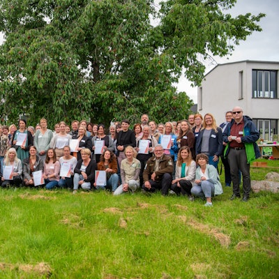 Eine Gruppe von Menschen steht auf einer Wiese unter einem Kirschbaum, mit dabei Josefine Paul (Grüne) Landesministerin für Kinder, Jugend, Familie, Gleichstellung, Flucht und Integration.