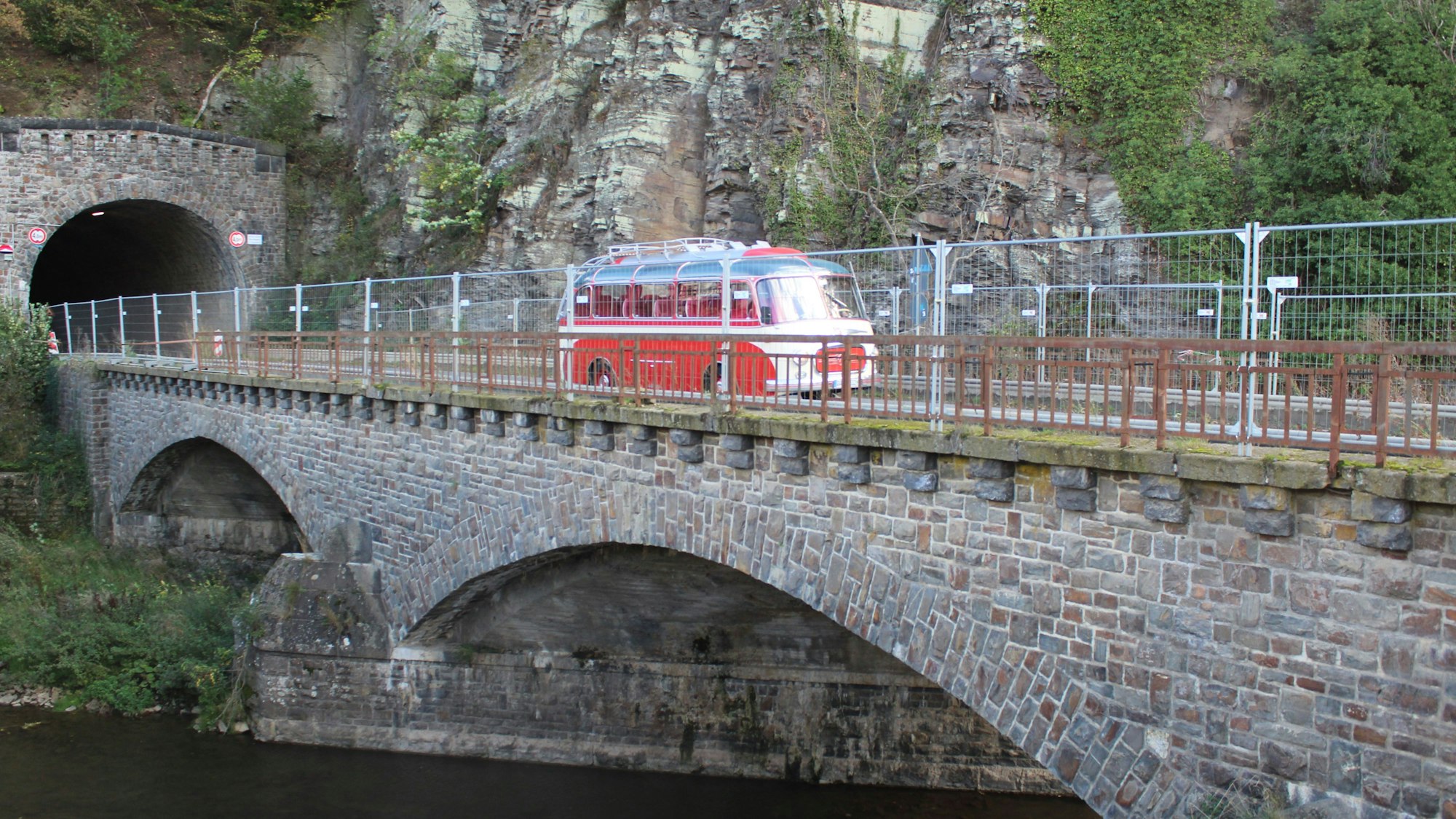 Ein roter Oldtimer-Bus fährt über eine Brücke.
