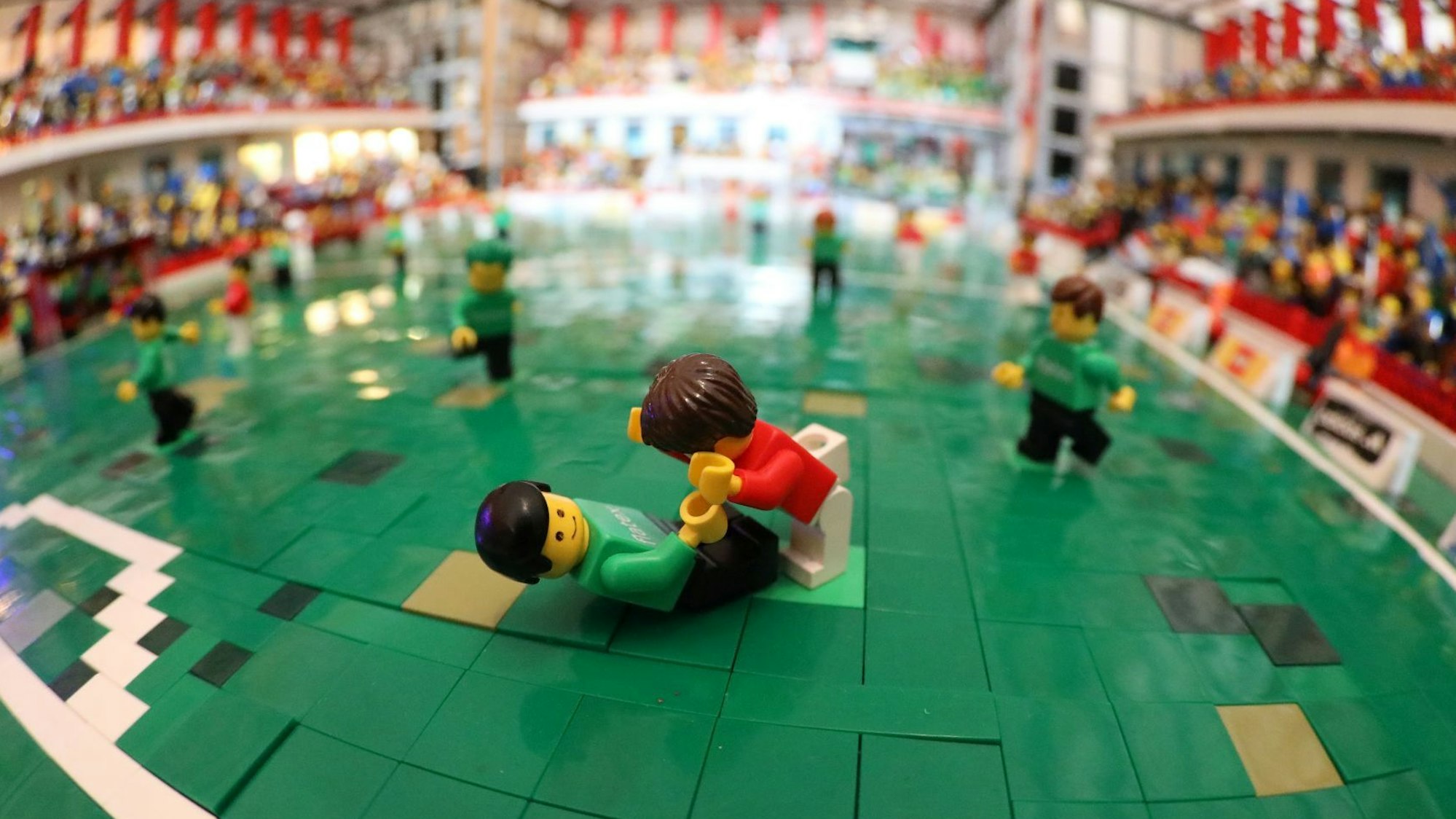 Grüne Plättchen bilden den Rasen des Stadion-Modells, auf dem kleine Figuren platziert sind.