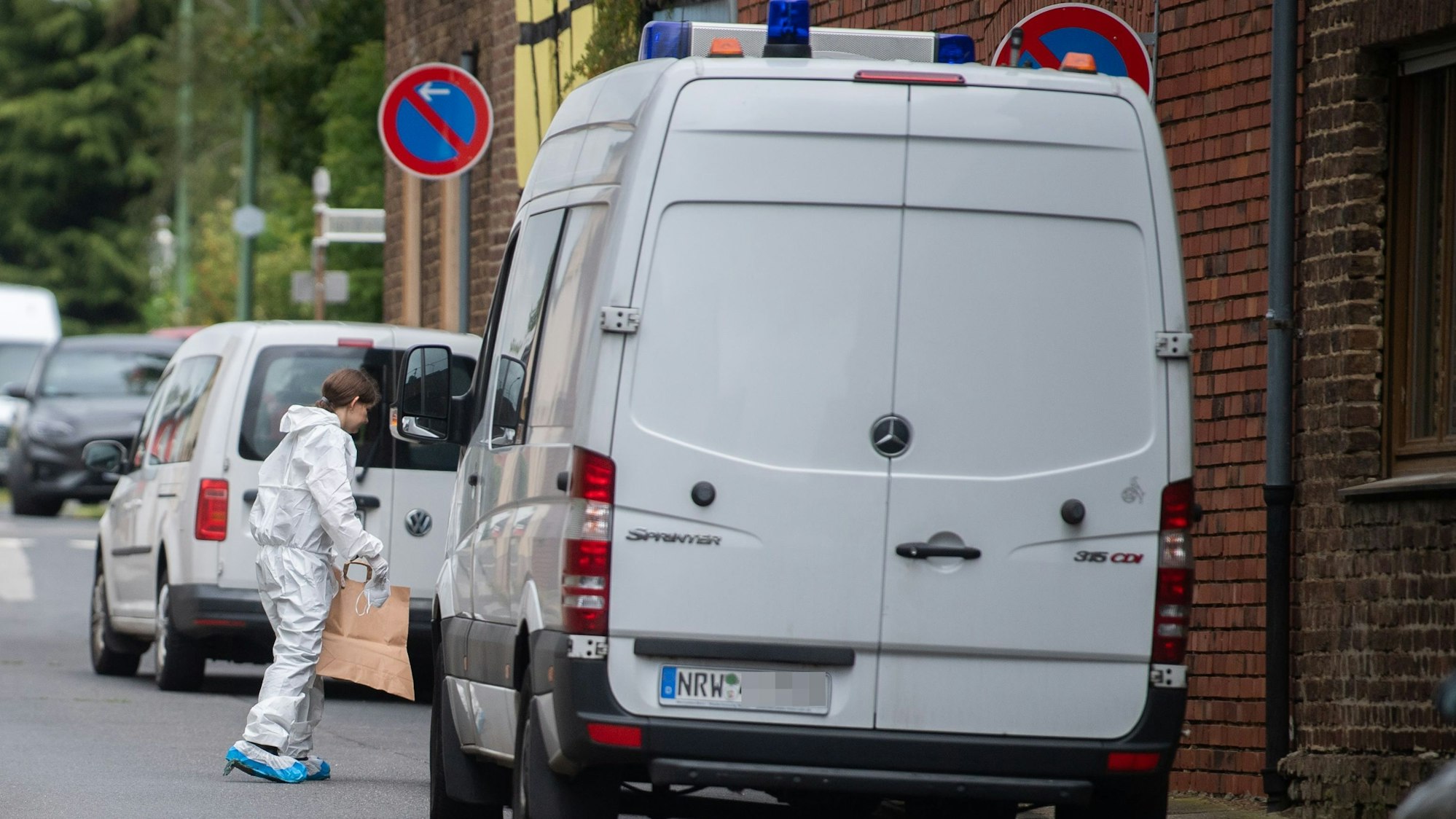 Ein Transporter der Polizei steht an der Straße, eine Frau im weißen Overall steht vor der Fahrertür.