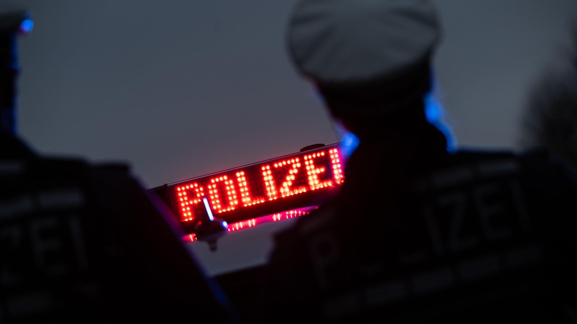 Zwei Polizisten stehen vor einem Polizeifahrzeug.
