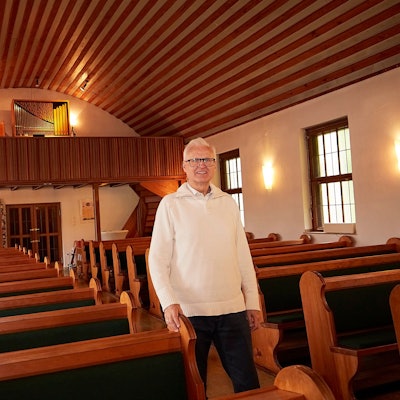 Pfarrer Christoph Cäsar geht durch den Mittelgang der evangelischen Kirche in Blankenheim. Rechts und links sind Bankreihen zu sehen, im Hintergrund die Orgel.