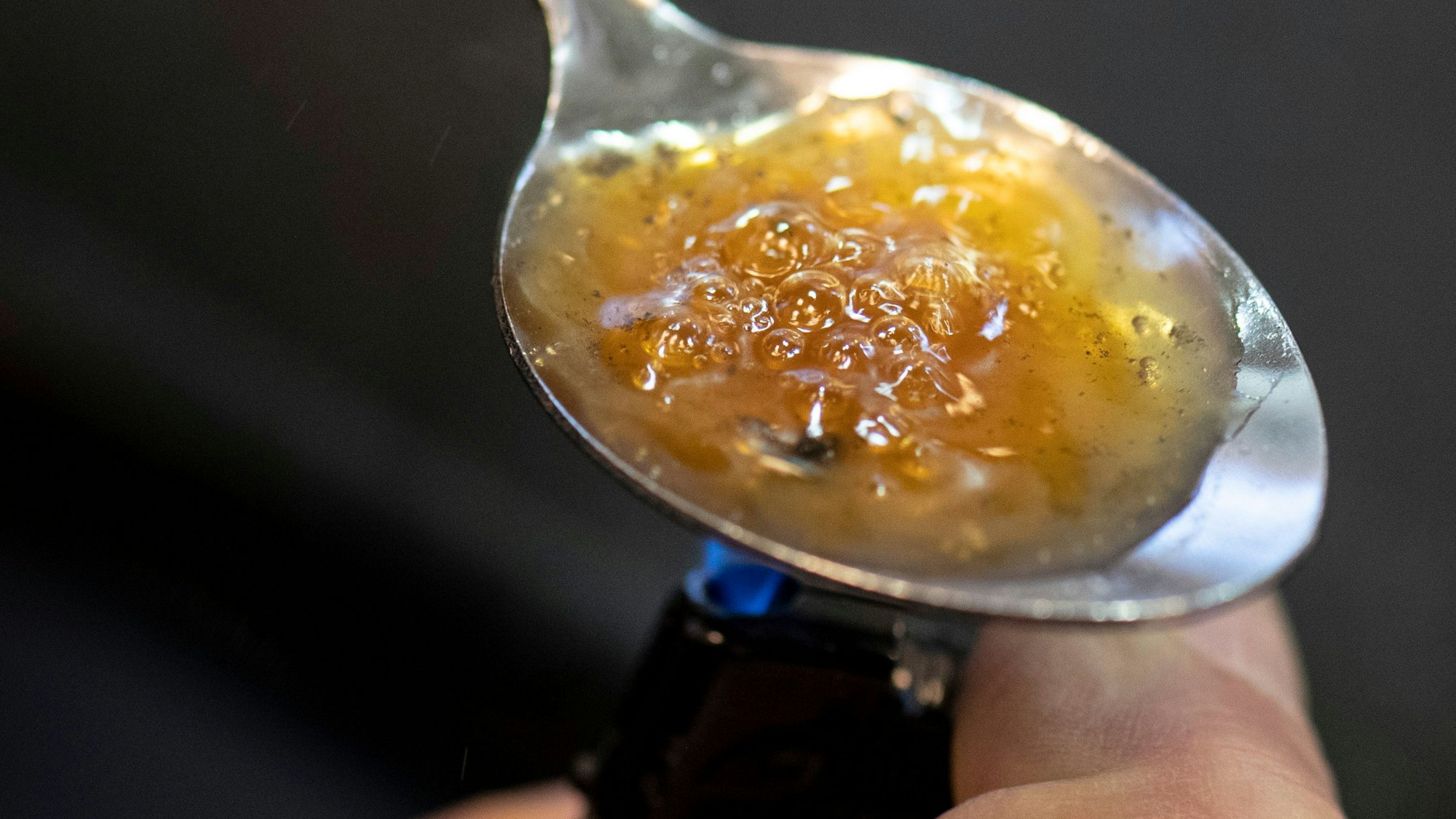 Ein Löffel mit einer bräunlichem Masse wird über eine Flamme gehalten.