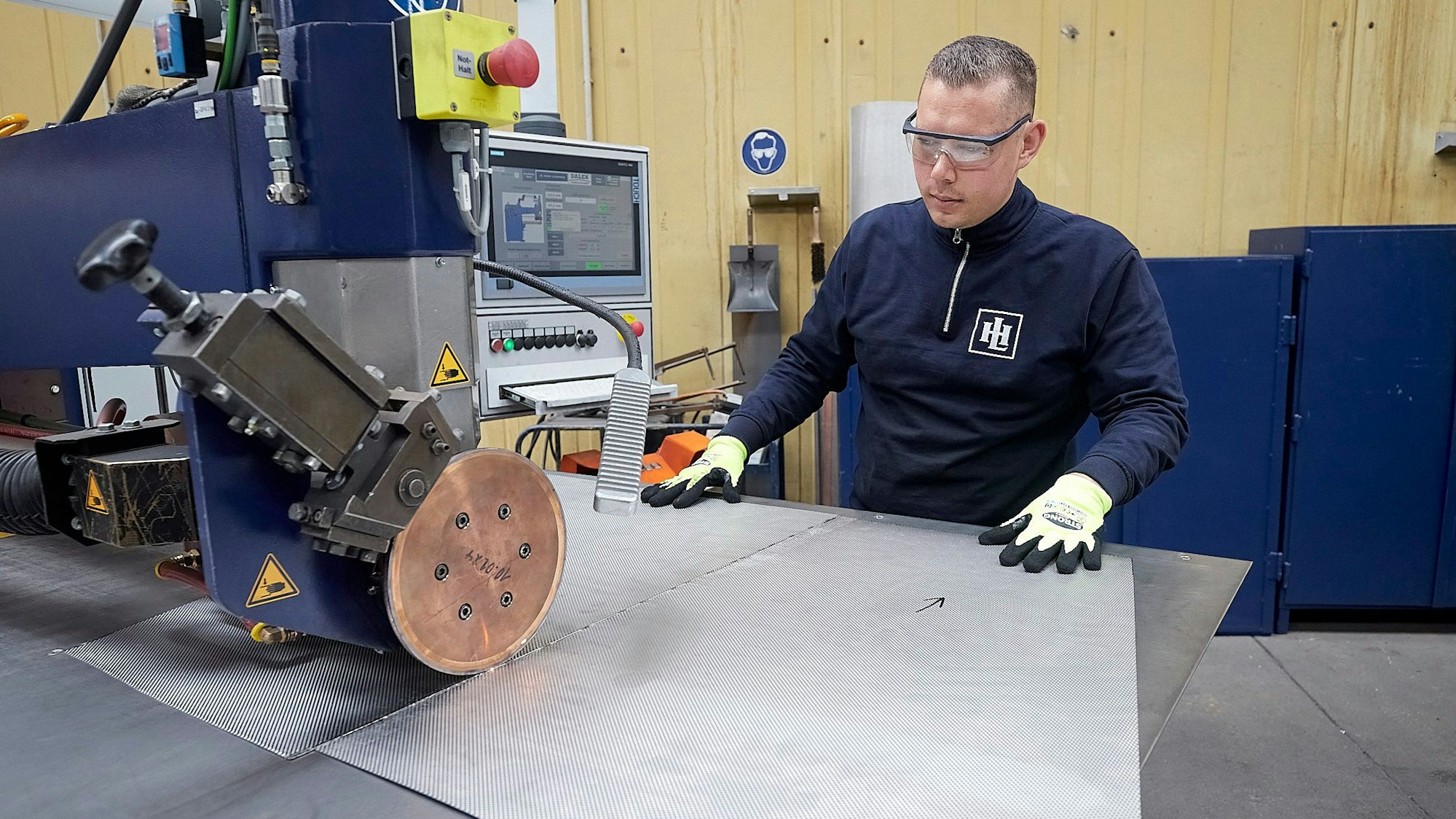 Ein Mitarbeiter steht an einer Maschine der Firma Hein, Lehmann in Zingsheim und bearbeitet ein Blech.