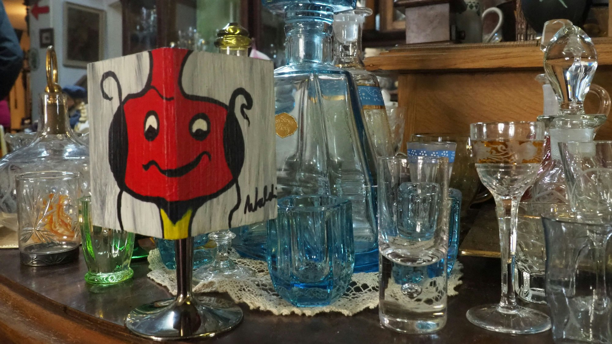 Auf einen Würfel ist ein rotes Gesicht gemalt, daneben stehen alte Gläser.