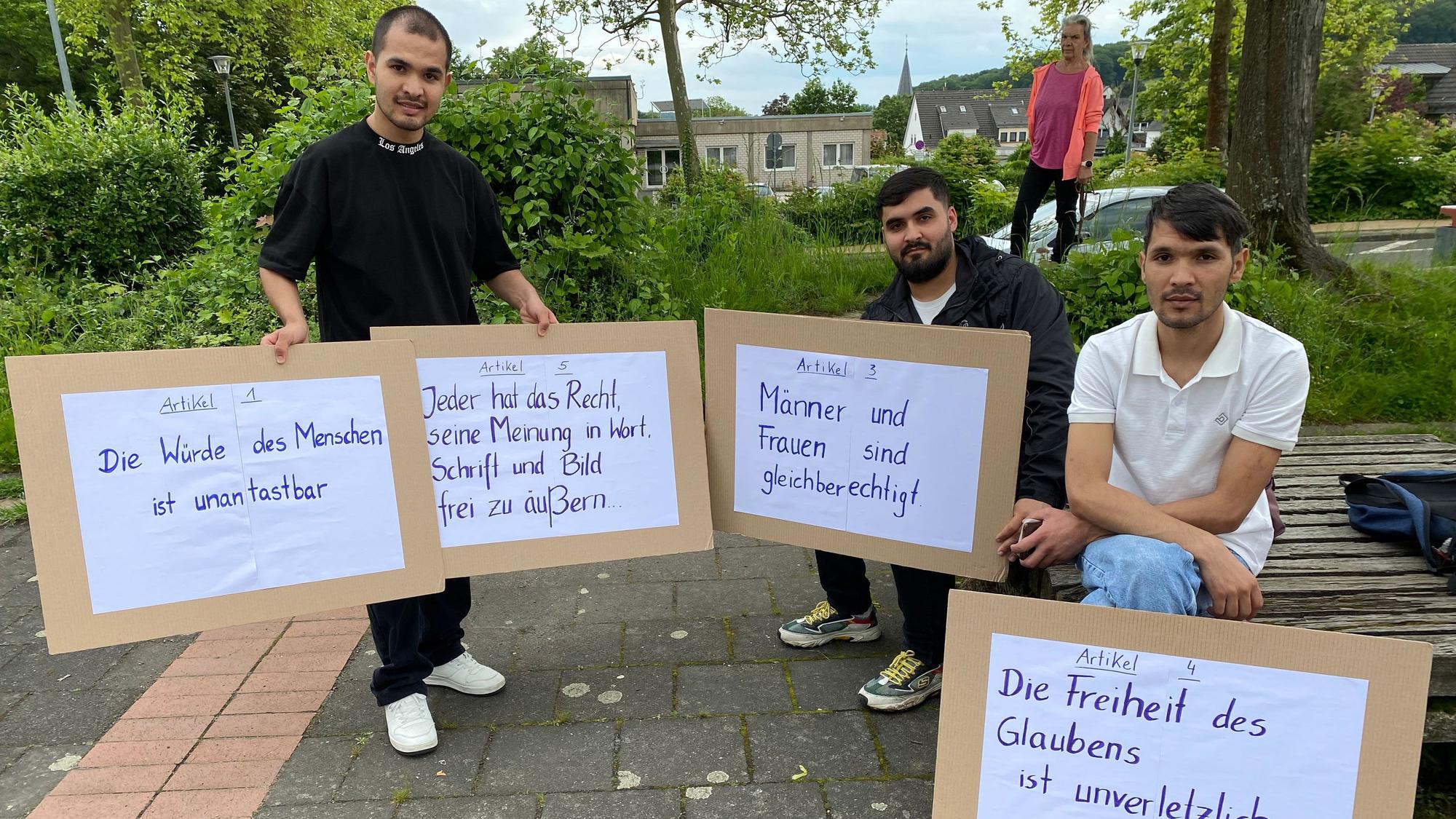 Geflüchtete, die im Ökumenischen Arbeitskreis aktiv sind, haben Schilder mit Artikeln des Grundgesetzes mit zur Kundgebung in Berkum gebracht.