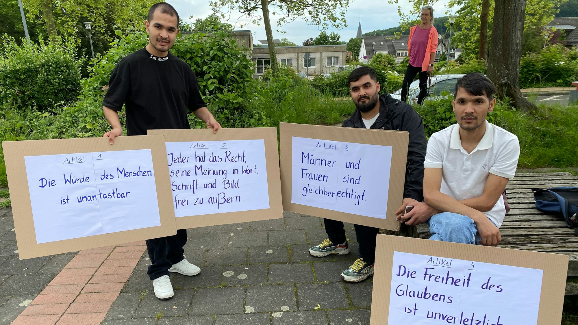 Geflüchtete, die im Ökumenischen Arbeitskreis aktiv sind, haben Schilder mit Artikeln des Grundgesetzes mit zur Kundgebung in Berkum gebracht.