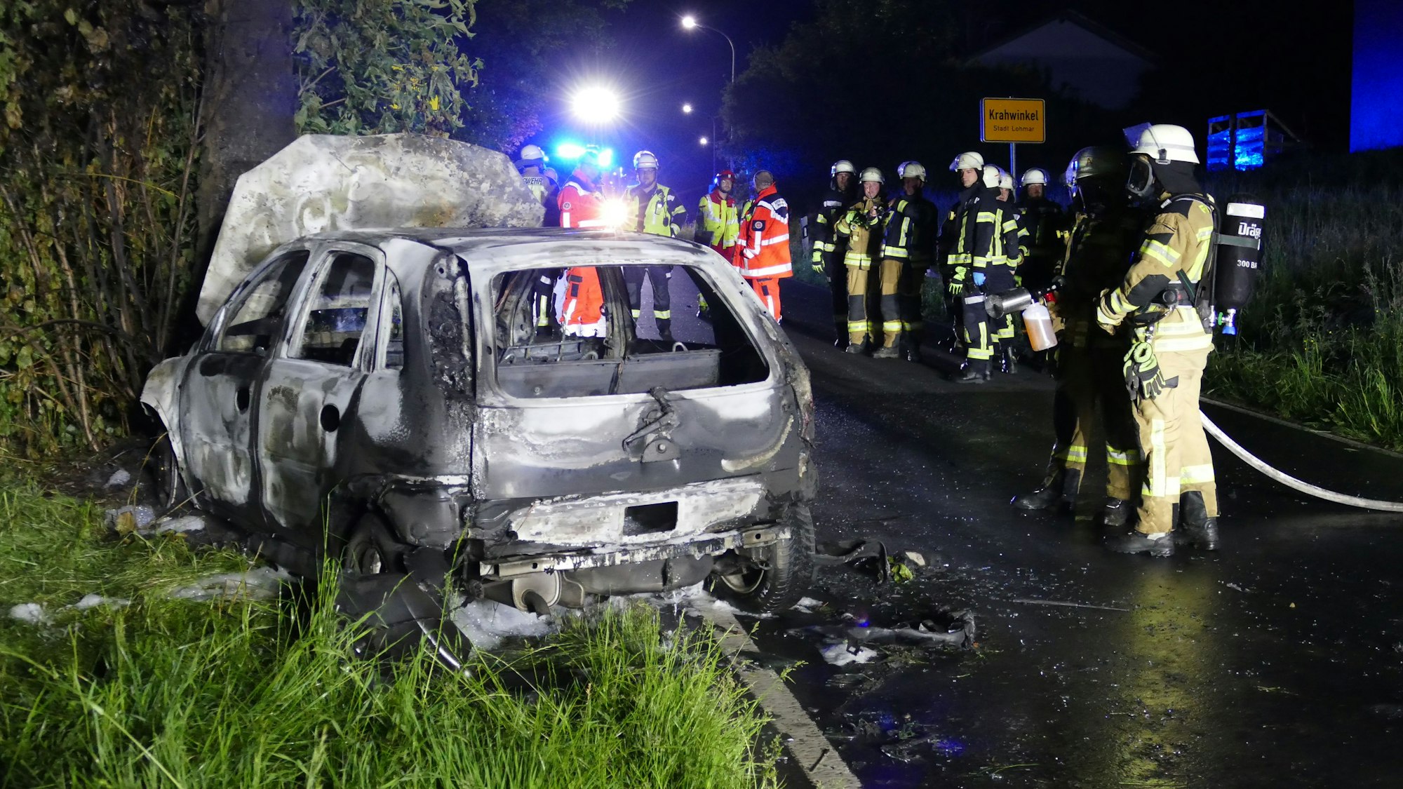Feuerwehrleute stehen vor einem ausgebrannten Auto.