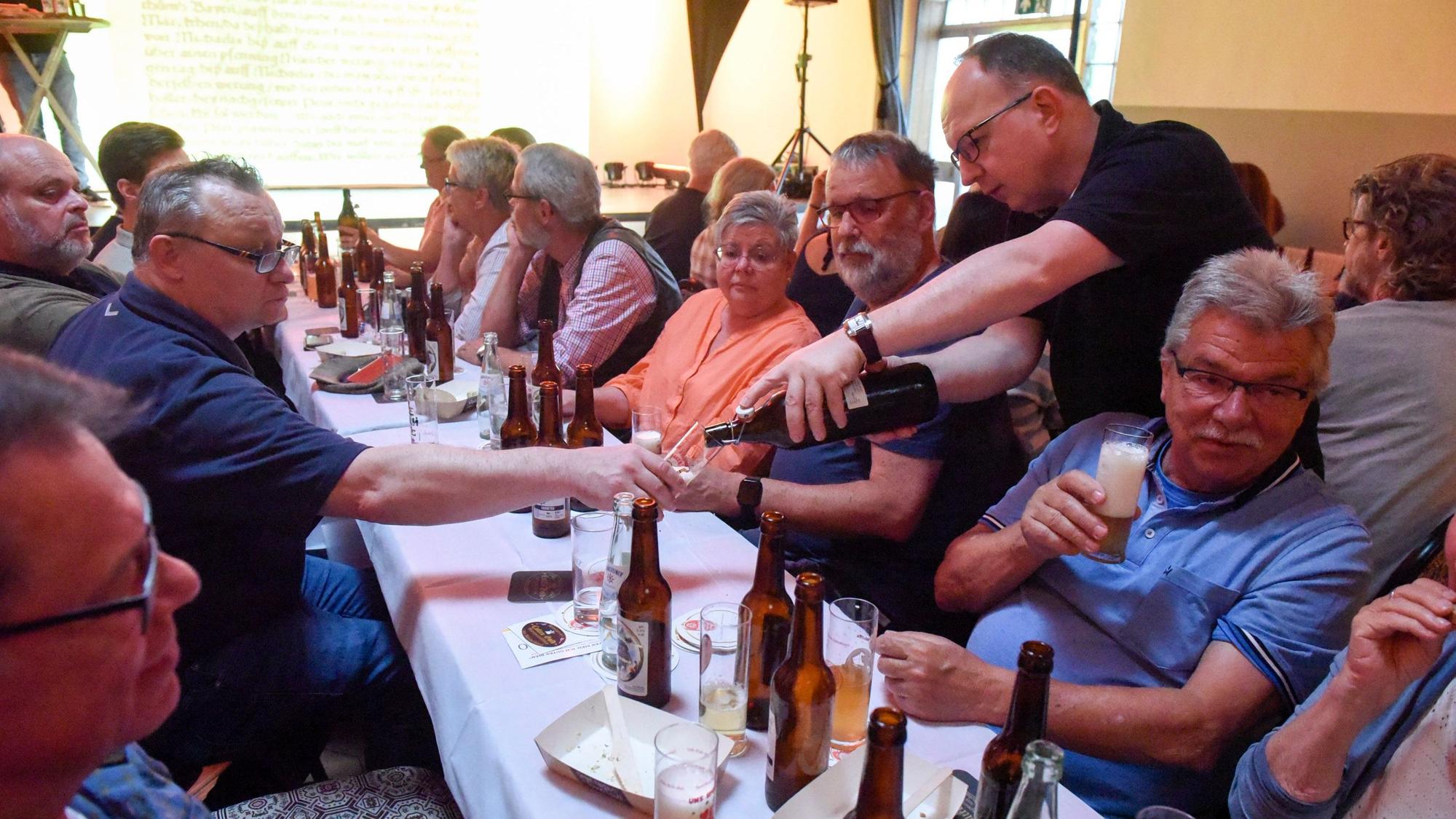 Frauen und Männer sitzen an einem Tisch, Anlass ist ein Biertasting.