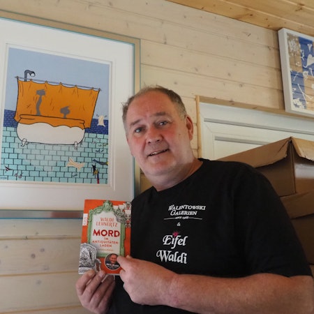 Walter Lehnertz steht mit seinem Buch vor einem seiner Bilder.