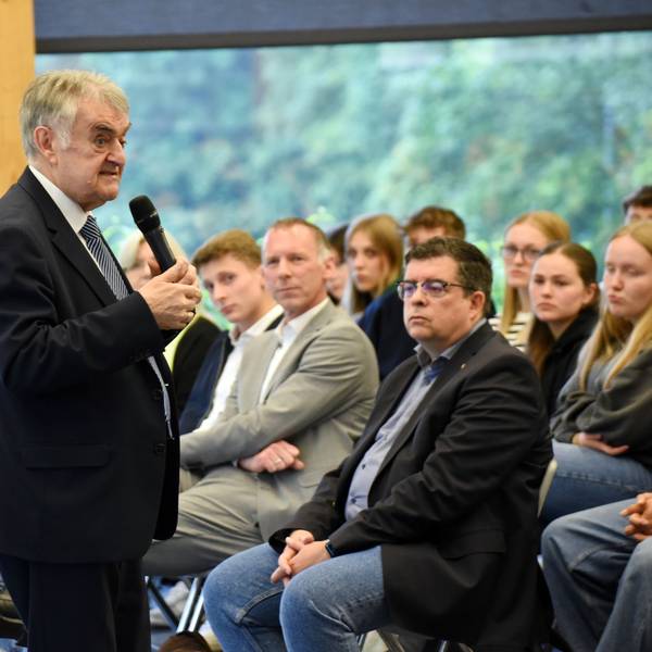Minister Reul steht mit einem Mikro vor der Schülerschaft. In der ersten Reihe sitzt der Bürgermeister.