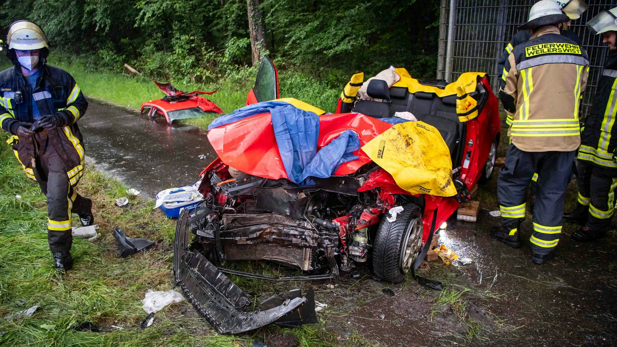 Das Bild zeigt das schwer demolierte Auto. Feuerwehrleute stehen um den Pkw herum.
