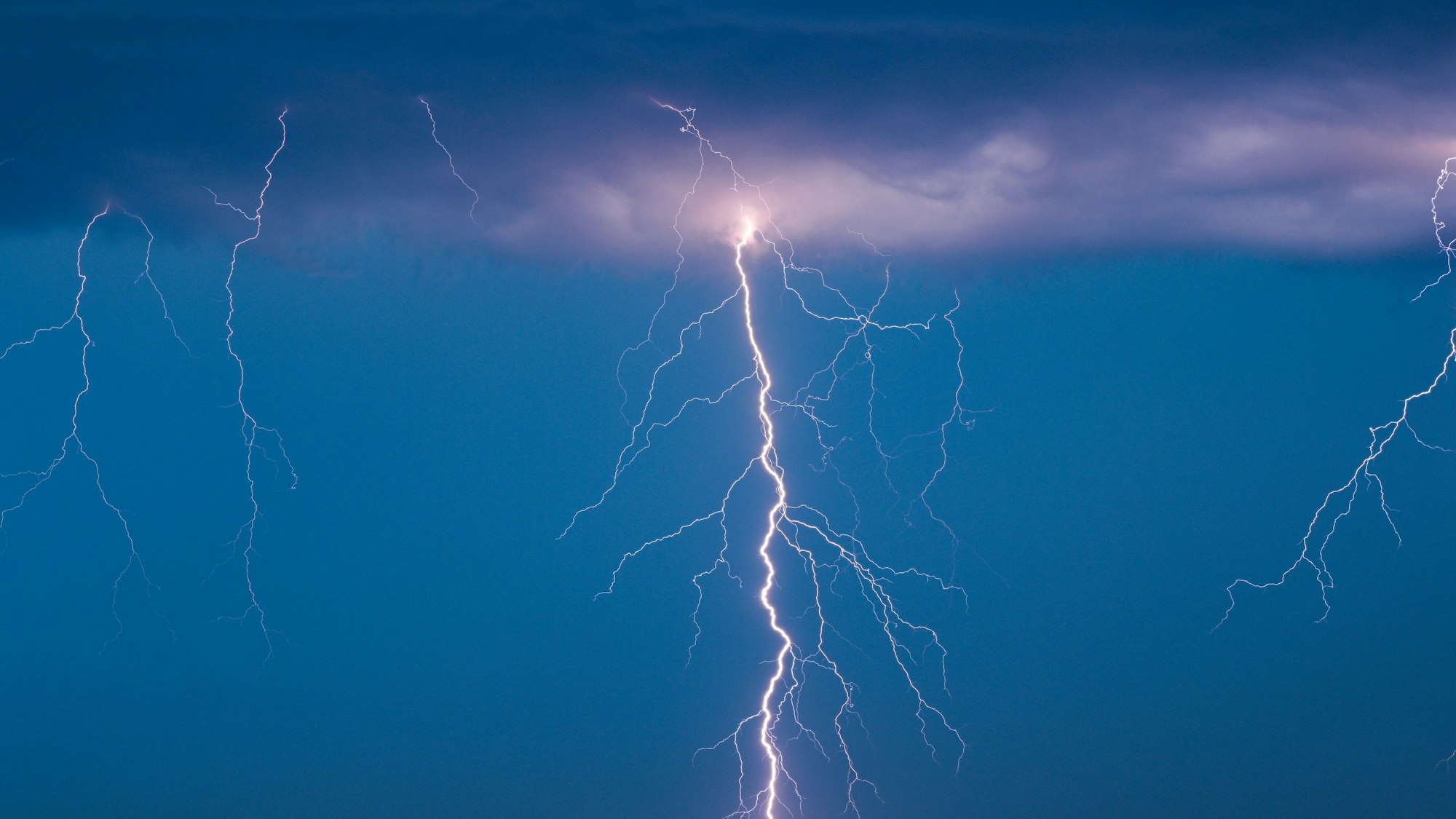Man sieht eine Gewitterwolke aus der gleichzeitig mehrere Blitze hervortreten und in den Boden einschlagen. (Symboldbild)