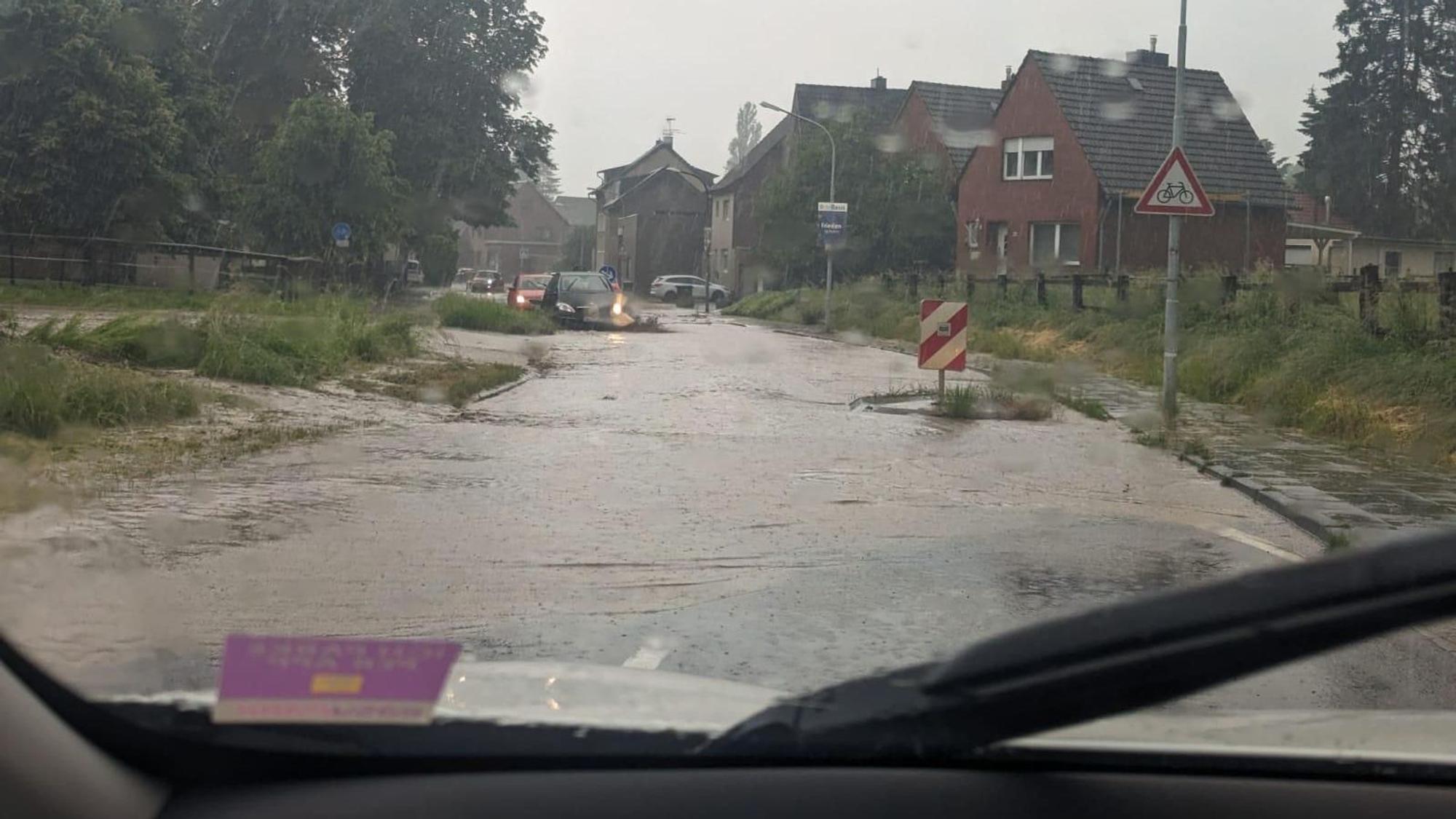 Wassermassen strömen über eine Straße in ein Dorf hinein.