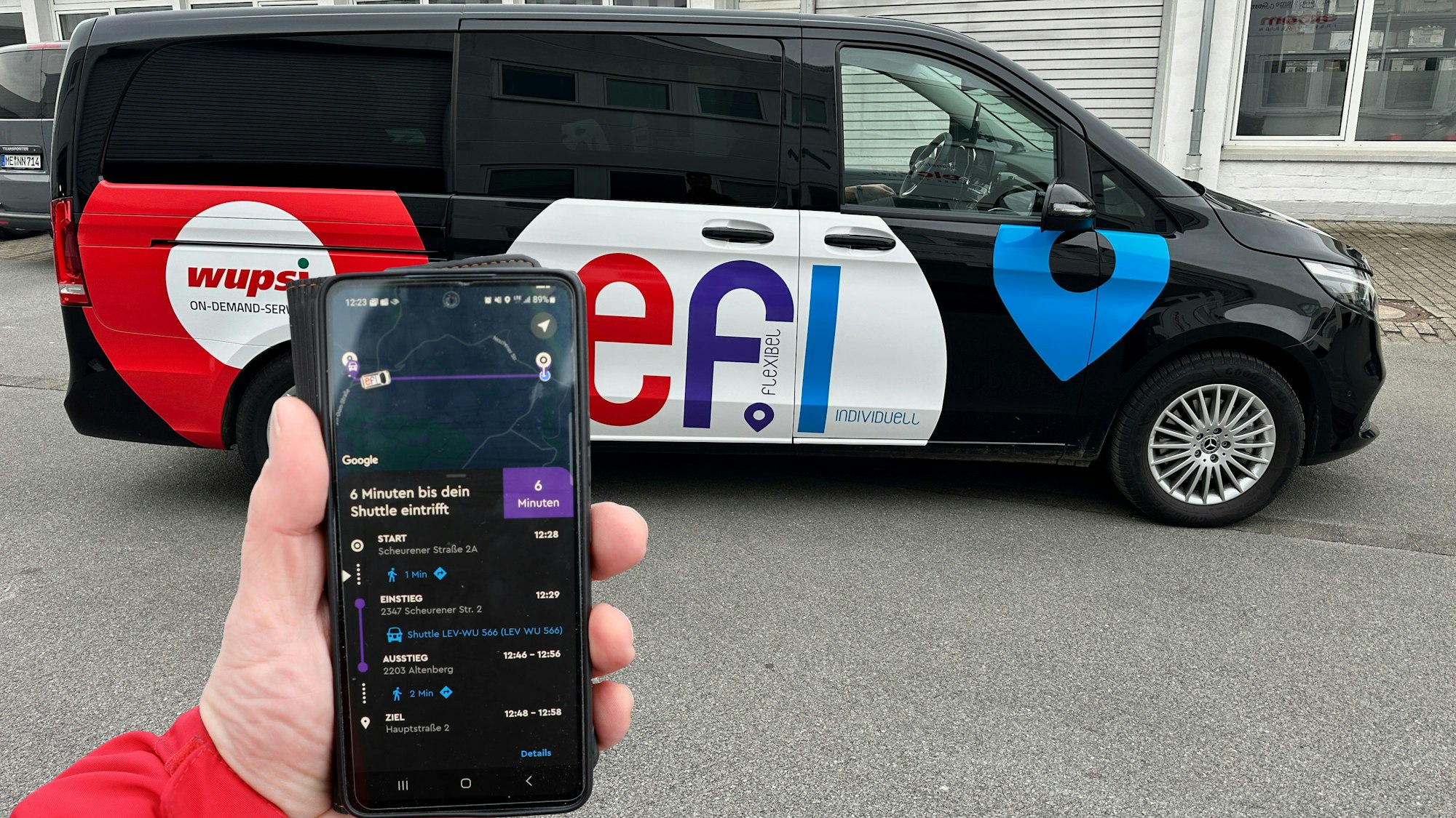Eine Hand mit Handy ist vor einem „Efi“-On-Demand-Verkehrs-Fahrzeug zu sehen.