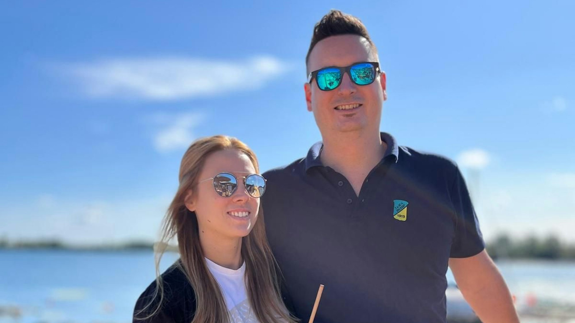 Eikamps Maikönigspaar Basti und Janna Stüber stehen vor einem blauen Himmel und schauen mit verspiegelten Sonnenbrillen in die Kamera.