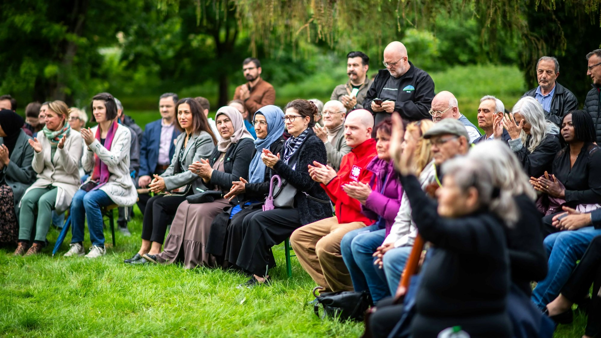 Die meisten Teilnehmerinnen und Teilnehmer sitzen nebeneinander auf Stühlen, andere stehen.