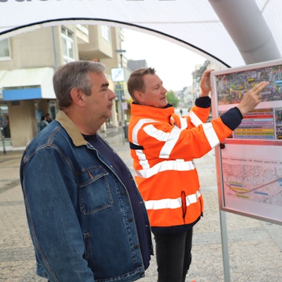 Zu sehen ist Helge Wego, der einem Bürger einen Bauplan erläutert.