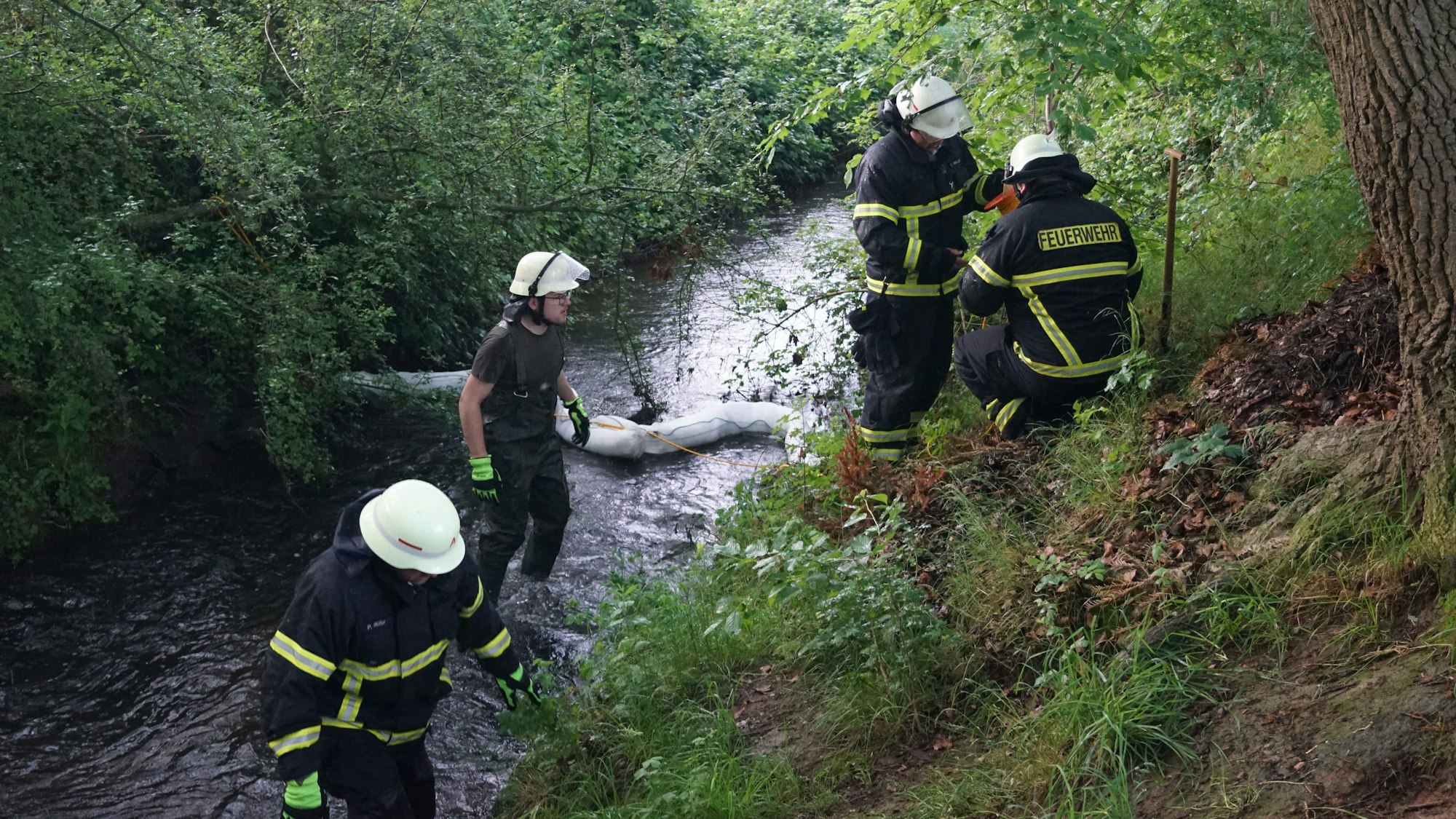Feuerwehrleute waten durch den Bach, in dem sie mit einem Feuerwehrschlauch eine Sperre errichtet haben.