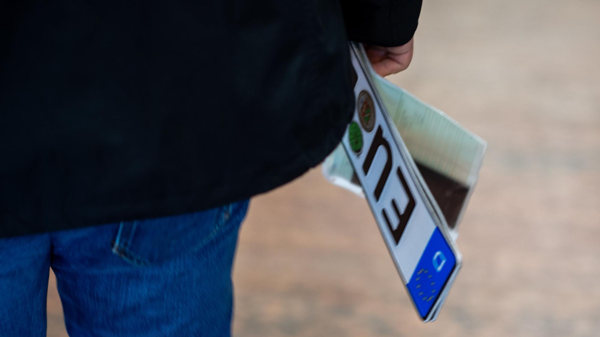Ein Mann trägt Nummernschild und Papiere in der rechten Hand.
