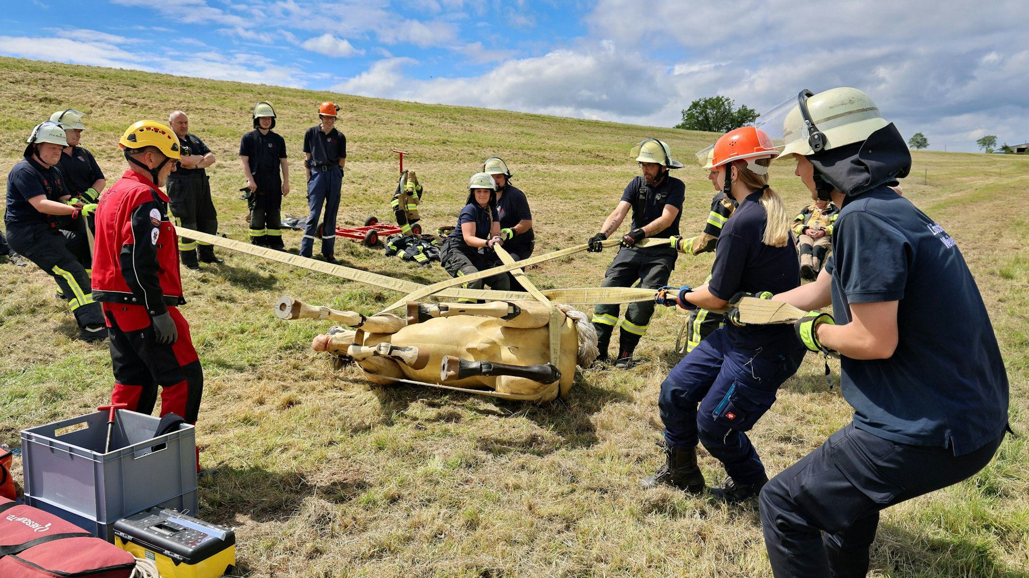 Mithilfe von Bändern drehen acht Feuerwehrleute den liegenden Pferdedummy langsam und kontrolliert auf die andere Seite. Trainer Lutz Hauch gibt Anweisungen.