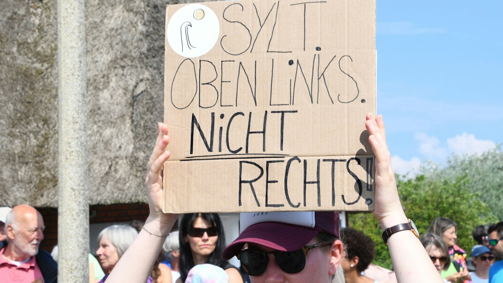 „Sylt oben links nicht rechts“, steht auf einem Plakat, das eine Frau bei einer Mahnwache am Sonntag auf Sylt in der Hand hält. In Kampen hatten sich laut Polizei rund 80 Menschen anlässlich des Rassismus-Eklats um ein Partyvideo auf Sylt versammelt.