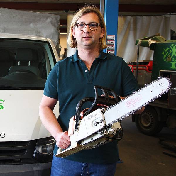 Sven Bung steht mit einer Motorsäge in einer Firmenhalle, links neben ihm ein Firmenwagen mit der Aufschrift „www.vitaforst.de“